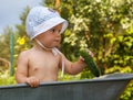 Smart toddler with cucumber in garden barrow