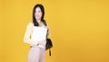 Smart university student Asian woman school bag holding laptop computer looking at something over isolated yellow background. Royalty Free Stock Photo