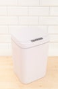 Smart waste basket. Electronic gadget for the home. The cover is closed. On a wooden floor. White tile background. View from above