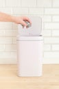 Smart waste basket. Electronic gadget for the home. The cover is open. Man`s hand throws trash. On a wooden floor. White tile