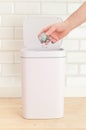 Smart waste basket. Electronic gadget for the home. The cover is open. Man`s hand throws trash. On a wooden floor. White tile