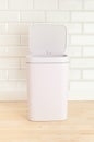 Smart waste basket. Electronic gadget for the home. The cover is open. On the wooden floor. White tile background