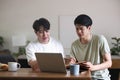 A smart young Asian male college student is tutoring and explaining something in a book to his friend while studying at Royalty Free Stock Photo