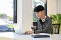 Smart young Asian male programmer or web developer sipping morning coffee while using laptop Royalty Free Stock Photo