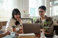 A smart young Asian male student in glasses is doing a co-project on a laptop in a coffee shop Royalty Free Stock Photo