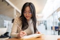 A smart young Asian woman doing her homework, or working remotely at a coffee shop Royalty Free Stock Photo