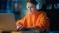 Smart Young Boy in Headphones Using Laptop Computer in a Dark Cozy Room at Home. Happy Teenager Royalty Free Stock Photo