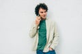 Smart young man smiling and talking on mobile phone with his friend against white cocnrete wall. Handsome male with curly hair Royalty Free Stock Photo