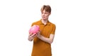 smart young red-haired caucasian male student with a tattoo dressed in a mustard t-shirt is holding a piggy bank Royalty Free Stock Photo