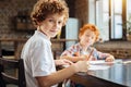 Smart youngster looking into camera while drawing with younger brother