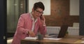 Smartly dressed asian businessman sitting at desk using laptop taking notes