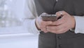 Smartly dressed man holding smartphone in hands, scrolling social media newsfeed