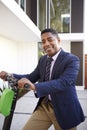 Smartly dressed middle aged African American man standing on electric scooter in front of his house, close up