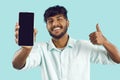 Smartphone with black blank screen in hand of happy man showing thumb up on light blue background.