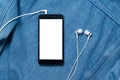 Smartphone with black case and a blank white screen and plugged in headphones ear buds on the background of denim Royalty Free Stock Photo