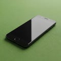 A smartphone with a black screen rests on a textured green surface. Its sleek design Royalty Free Stock Photo
