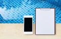 Smartphone with blank paper sheet on wooden clipboard over clean swimming pool water Royalty Free Stock Photo