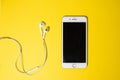 Smartphone with Blank Screen Connects to Earphones with Spiral Cable on yellow Background Top View