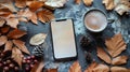 A smartphone with a blank screen lies on a rustic table surrounded by autumn leaves, pine cones, and a cup of coffee Royalty Free Stock Photo