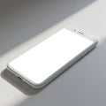 A smartphone with a blank white screen lies on a smooth, flat surface partially Royalty Free Stock Photo