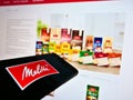 Smartphone with business logo of German coffee retail company Melitta on display in front of web page.