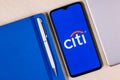 Smartphone with Citigroup logo on wooden table next to laptop and business planner