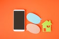 Smartphone with clipping path on touchscreen,  house paper cut and couple bubble speech paper on orange background and copy space Royalty Free Stock Photo