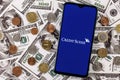 Smartphone with Credit Suisse bank logo surrounded by variety of metal coins on background of dollar bills