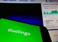 Smartphone with Duolingo language app logo on screen and blurred background with Nasdaq stock index chart. Duolingo will go public