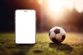 Smartphone with empty white screen for mockup and soccer ball on field grass at sunset closeup. Internet sports betting Royalty Free Stock Photo