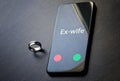 The smartphone that the ex-wife is calling lies on a dark surface next to the wedding ring. Relationship of former spouses after