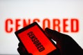 A smartphone in hand displaying the `censored` text. Same text in red blurred on white background. The concept of censorship