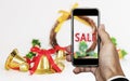 Smartphone on hand with `SALE` on screen, with Christmas decorations ornament, Holiday Christmas Sale