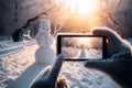 A smartphone in the hands of a tourist taking a photo of a friendly snowman in a city park on a frosty winter day Royalty Free Stock Photo