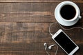 Smartphone with headphones and a cup with coffee on a brown wooden table. view from above