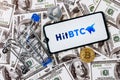 A smartphone with the HitBTC logo, a shopping cart and a cryptocoins on the dollar bills