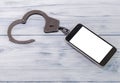 Smartphone, iron handcuffs on a wooden background. Royalty Free Stock Photo