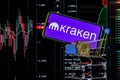 A smartphone with the Kraken logo in shopping cart on the background of the live trading webpage. Kraken dashboard