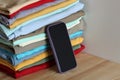 Smartphone leaning on stack of folded clothes on wooden table Royalty Free Stock Photo