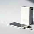 A smartphone lies horizontally, connected via a cable to a rectangular white power Royalty Free Stock Photo