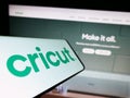 Smartphone with logo of American cutting plotter company Cricut Inc. on screen in front of website.