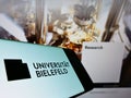Smartphone with logo of German education institution Bielefeld University on screen in front of webpage.