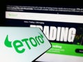 Smartphone with logo of Israeli social trading company eToro on screen in front of business website.