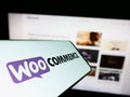 Smartphone with logo of open-source e-commerce solution WooCommerce on screen in front of business website.