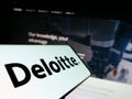 Smartphone with logo of professional services company Deloitte on screen in front of business website.