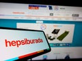 Smartphone with logo of Turkish e-commerce platform Hepsiburada on screen in front of business website.