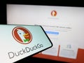 Smartphone with logo of US Internet search engine DuckDuckGo (DDG) on screen in front of company website.