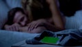 Smartphone lying on bed, lady kissing sleepy male on background, green screen