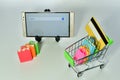 Smartphone, a miniature shopping trolley with miniature bags and a card in it on a white surface