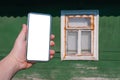 Smartphone mockup in male hand. Against the background of a wooden green wall of the house with an old white retro window Royalty Free Stock Photo